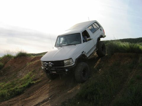 1985 Ford Bronco - White Ford Bronco navigates an off-road trail, demonstrating its climbing capability.