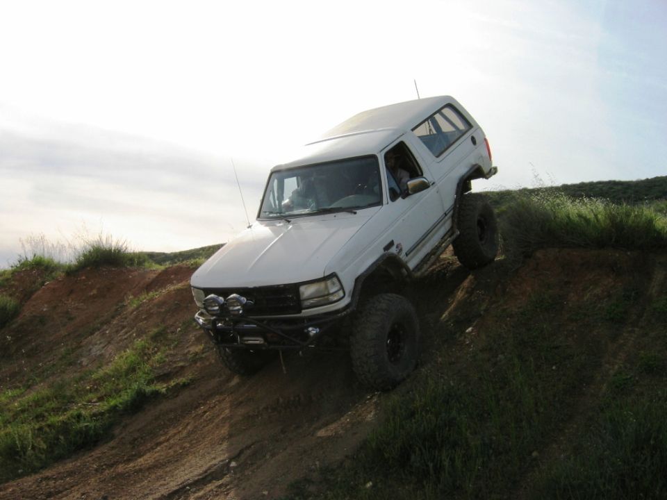 White lifted Ford Bronco on big tires climbing down a steep dirt hill off-road.