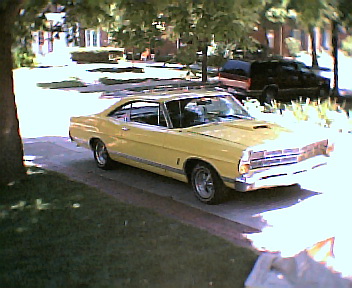 1967 Ford Galaxie - A yellow 1967 Ford Galaxie is parked on the side of a street with trees and houses in the background.