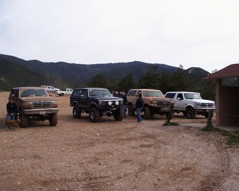 1993 Ford Bronco - Several Ford Bronco SUVs are parked outdoors on a dirt lot, with people and a dog nearby.