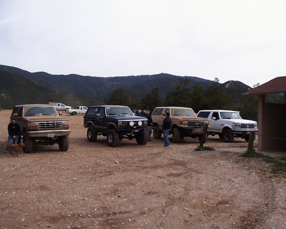 Four Ford Bronco SUVs parked on a dirt lot with hills in the background