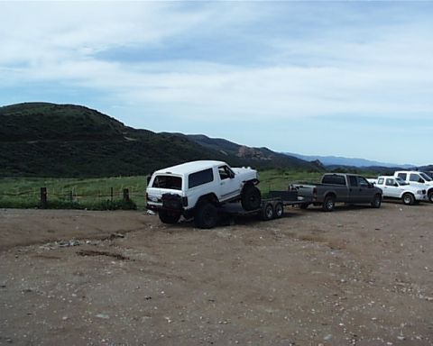 1993 Ford Bronco - A white SUV is being transported on a trailer, with several other vehicles visible in the background under a cloudy sky.