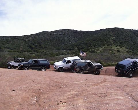 1993 Ford Bronco - Several SUVs, including a 1993 Ford Bronco, are parked on a dirt road with hills in the background.