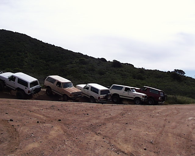 Five Ford Bronco SUVs parked on a dirt road with a hill in the background