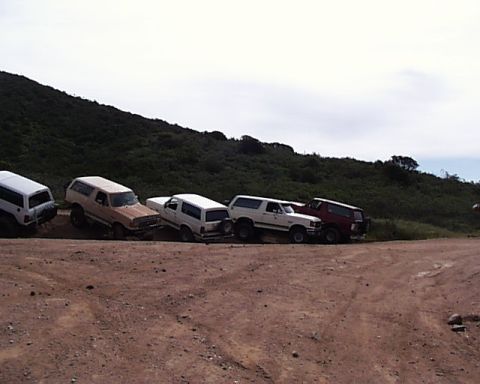 1993 Ford Bronco - Several Ford Bronco SUVs are parked on a dirt incline with a grassy hill in the background.