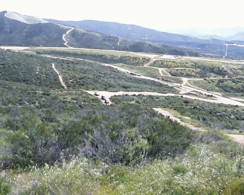 1993 Ford Bronco - A wide view of a hilly, green landscape with several off-road vehicles navigating dirt tracks.