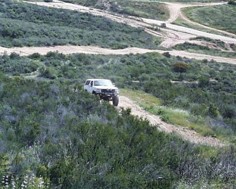 1993 Ford Bronco - White 1993 Ford Bronco navigates a dirt road in a natural, undeveloped landscape.