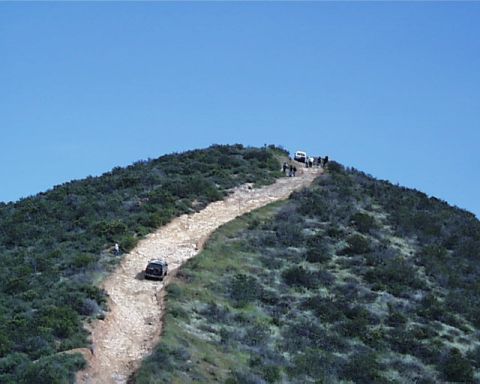1993 Ford Bronco - Multiple SUVs navigate a challenging off-road trail under a clear blue sky.