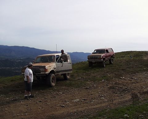 1993 Ford Bronco - Two Ford Broncos are parked on a dirt hill overlooking a valley, with one person standing next to the white Bronco.