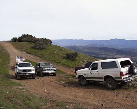 1993 Ford Bronco - A white 1993 Ford Bronco is parked on a dirt road with other vehicles and a scenic mountain backdrop.