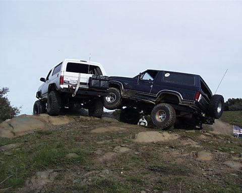 1993 Ford Bronco - Two SUVs navigate a challenging off-road course on a sunny day.