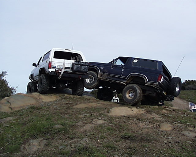 1993 Ford Bronco and a white SUV climbing a rocky hill
