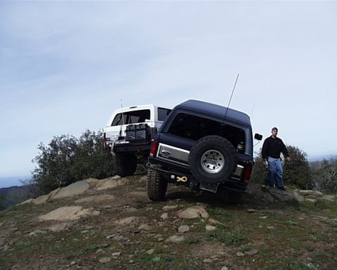 1993 Ford Bronco - Two off-road vehicles are parked on a rocky incline under a cloudy sky.