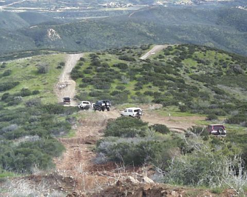 1993 Ford Bronco - Multiple off-road vehicles traverse a challenging dirt path winding through a hilly, green landscape.