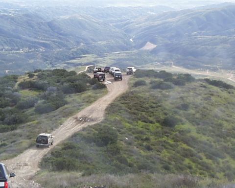 1993 Ford Bronco - A group of off-road vehicles navigates a winding dirt path amidst rolling hills.