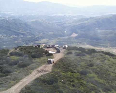 1993 Ford Bronco - A convoy of SUVs navigates a winding dirt road through a scenic mountain range.