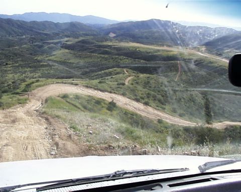 1993 Ford Bronco - View from inside a vehicle as it navigates a winding dirt road through a scenic, hilly terrain.