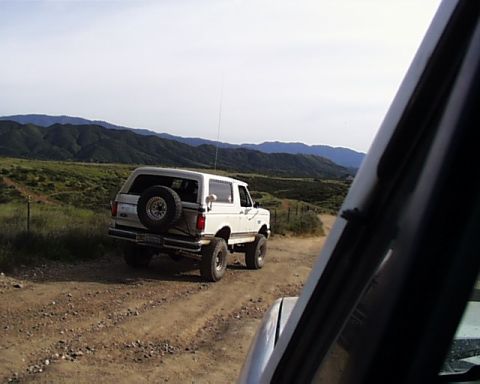 1993 Ford Bronco - White 1993 Ford Bronco driving on a dirt road through a hilly landscape.