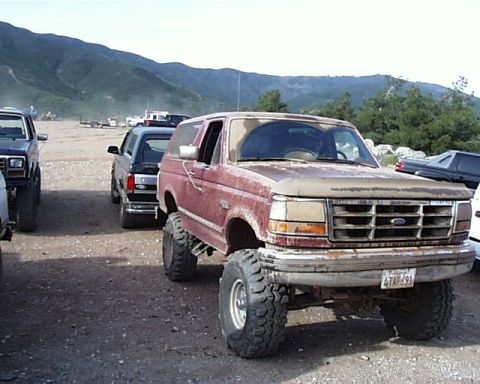 1993 Ford Bronco - A lifted 1993 Ford Bronco sits parked outdoors with other vehicles in the background.