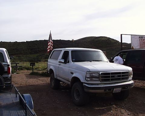 1993 Ford Bronco - White Ford Bronco parked outdoors with American flag flying. Another vehicle is visible to the right.