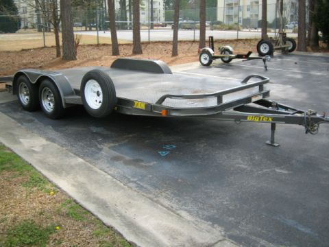 1996 Ford Bronco - A car hauler trailer is parked in a lot, with another smaller trailer and a piece of equipment in the background.