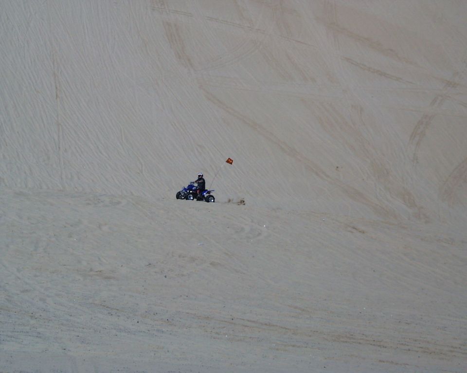 Blue ATV with rider and red flag on sand dune