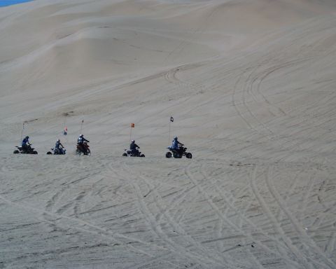 1993 Ford Bronco - A group of four-wheelers navigate the sandy terrain of a dune landscape, each marked with a colorful flag.
