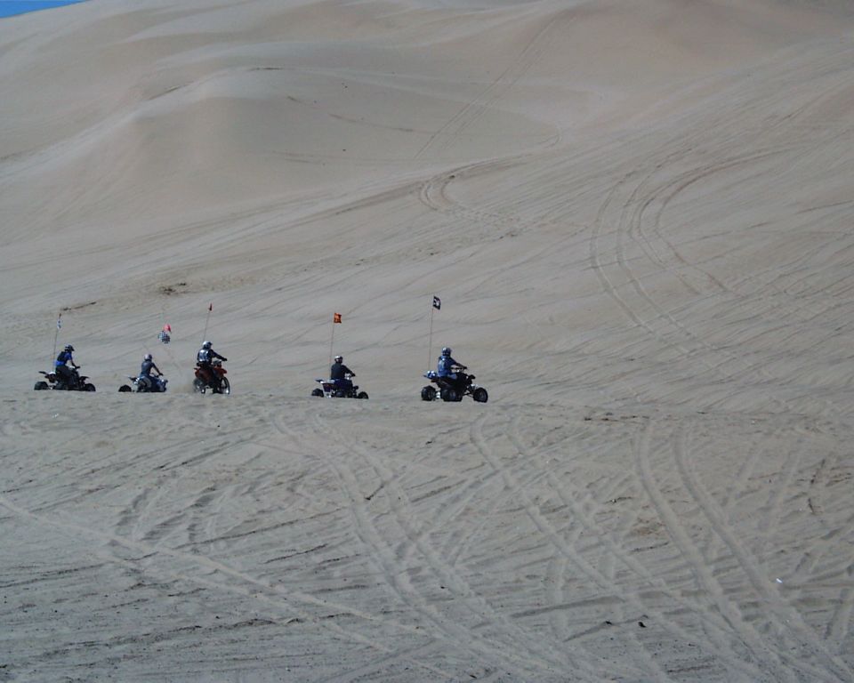 Four-wheelers with flags ride across sand dunes