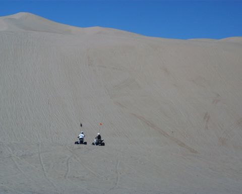 1993 Ford Bronco - Two ATVs are seen riding on a vast sand dune with tire tracks visible.