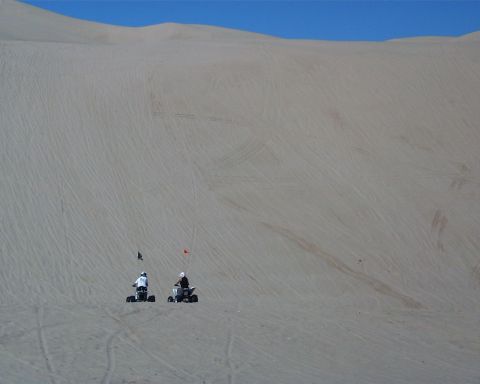 1993 Ford Bronco - Two ATVs navigate a large sand dune, leaving tracks in the sand.