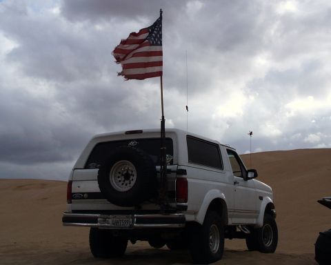 1993 Ford Bronco - White 1993 Ford Bronco with an American flag flying in the desert under a cloudy sky.