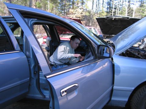 1991 Ford LTD Crown Victoria - A man works on the interior of a light blue sedan with its driver's door open, while another vehicle with its hood up is visible in the bac…