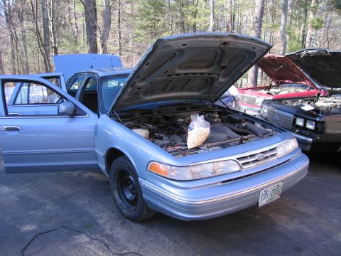 1991 Ford LTD Crown Victoria - A light blue sedan, possibly a 1992 model, sits with its hood and driver's door open, revealing its engine bay and a bag of snacks.