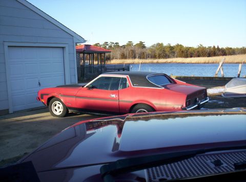 1995 Ford Bronco - A red Ford Mustang coupe is parked by a garage near a body of water.