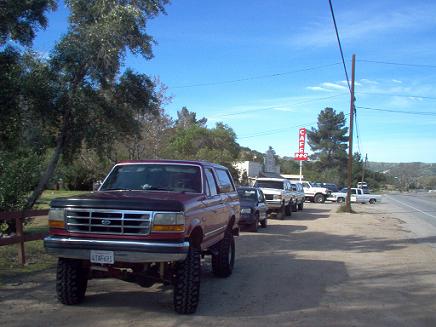 1988 Ford Bronco - A line of trucks are parked on the side of the road near a cafe.