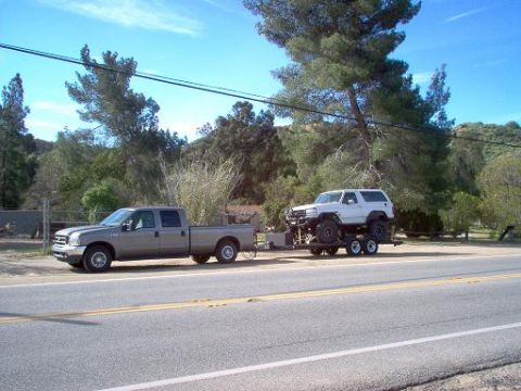 1988 Ford Bronco - A white 1988 Ford Bronco is transported on a trailer towed by a pickup truck on a sunny day.