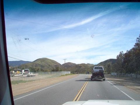 1988 Ford Bronco - A white Ford Bronco tows a trailer with a motorcycle on a highway, with hills in the background.