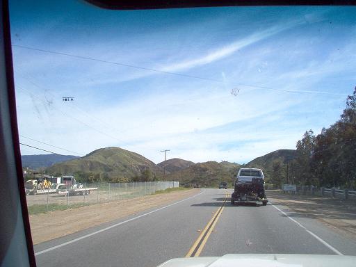 White Ford Bronco towing a trailer with a motorcycle, seen from behind on a highway