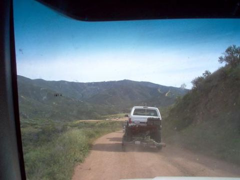 1988 Ford Bronco - Pickup truck towing a trailer on a dusty mountain road.