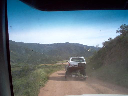 White pickup truck towing a trailer on a dirt road with mountains in the background