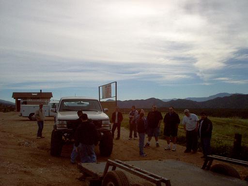 White Ford F-Series truck with a group of people around it. Another white truck is parked nearby