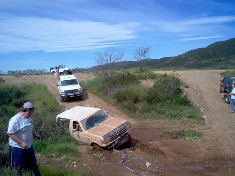1988 Ford Bronco - Multiple vehicles navigating a muddy off-road trail with a stuck Ford Bronco.