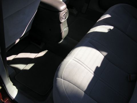 1998 Ford Taurus - Rear passenger compartment of a sedan shot through the open door, showing a clean gray cloth bench seat, black carpet with fitted floor mat…