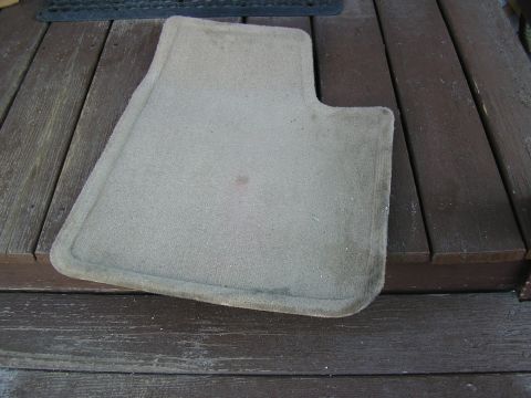 1998 Ford Taurus - A tan car floor mat rests on weathered wooden planks, showing some stains.