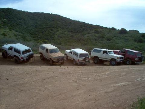 1988 Ford Bronco - Multiple Ford Broncos parked on a dirt road during an off-road excursion.