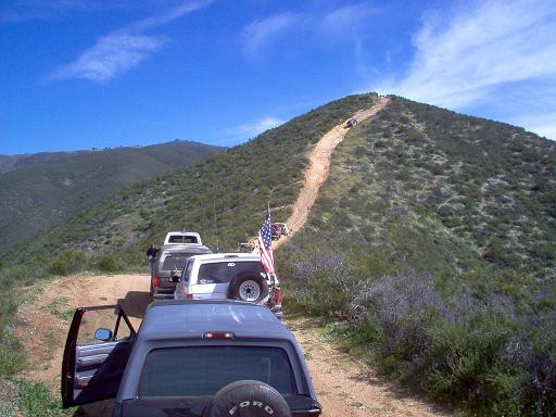 Dark blue Ford Bronco rear view with spare tire, open driver door, parked on dirt road