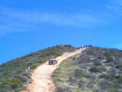 1988 Ford Bronco - A 1988 Ford Bronco navigates a steep dirt path on a sunny day with a clear blue sky.