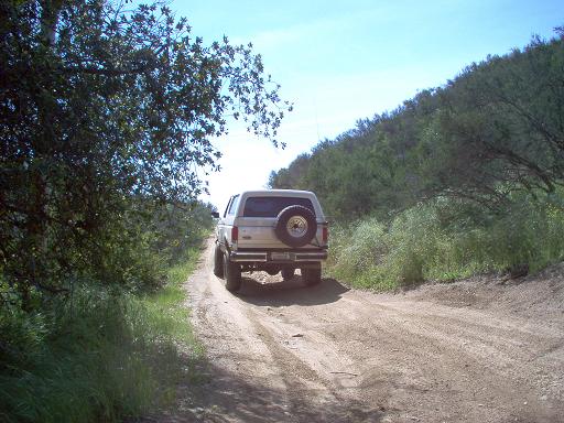 1988 Ford Bronco parked on a dirt road with trees and a hill in the background