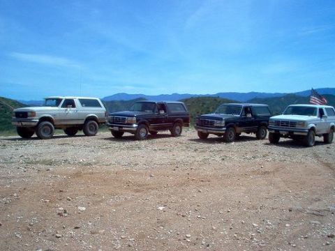 1988 Ford Bronco - Several Ford Bronco SUVs are lined up on a dusty, arid terrain under a clear blue sky.