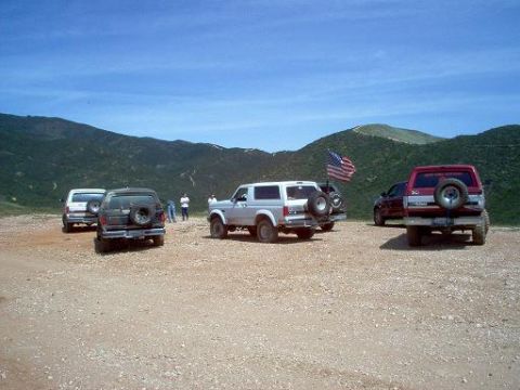 1988 Ford Bronco - A group of SUVs are parked in a dusty, outdoor area with hills under a clear blue sky.